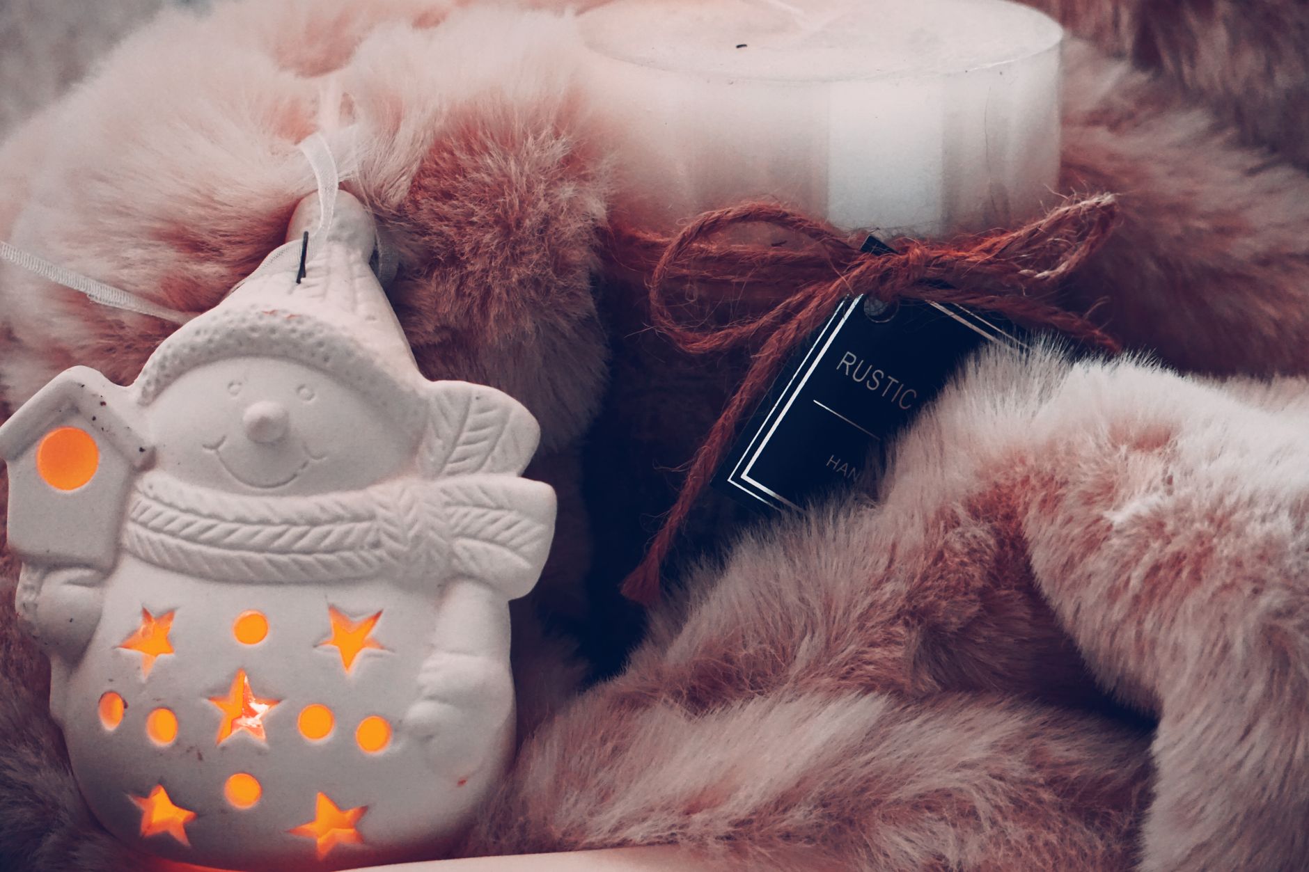 A festive snowman ornament beside a candle on a plush fur blanket, creating a warm winter ambiance.